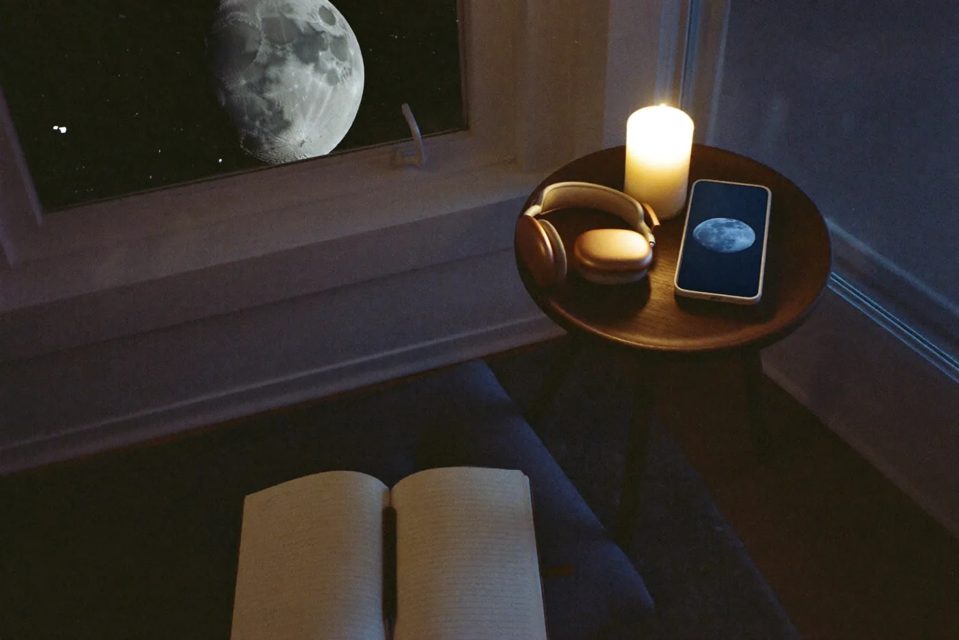 Un coin de nuit préparé pour l'écoute : bougie, écouteurs, carnet ouvert, la Lune à la fenêtre